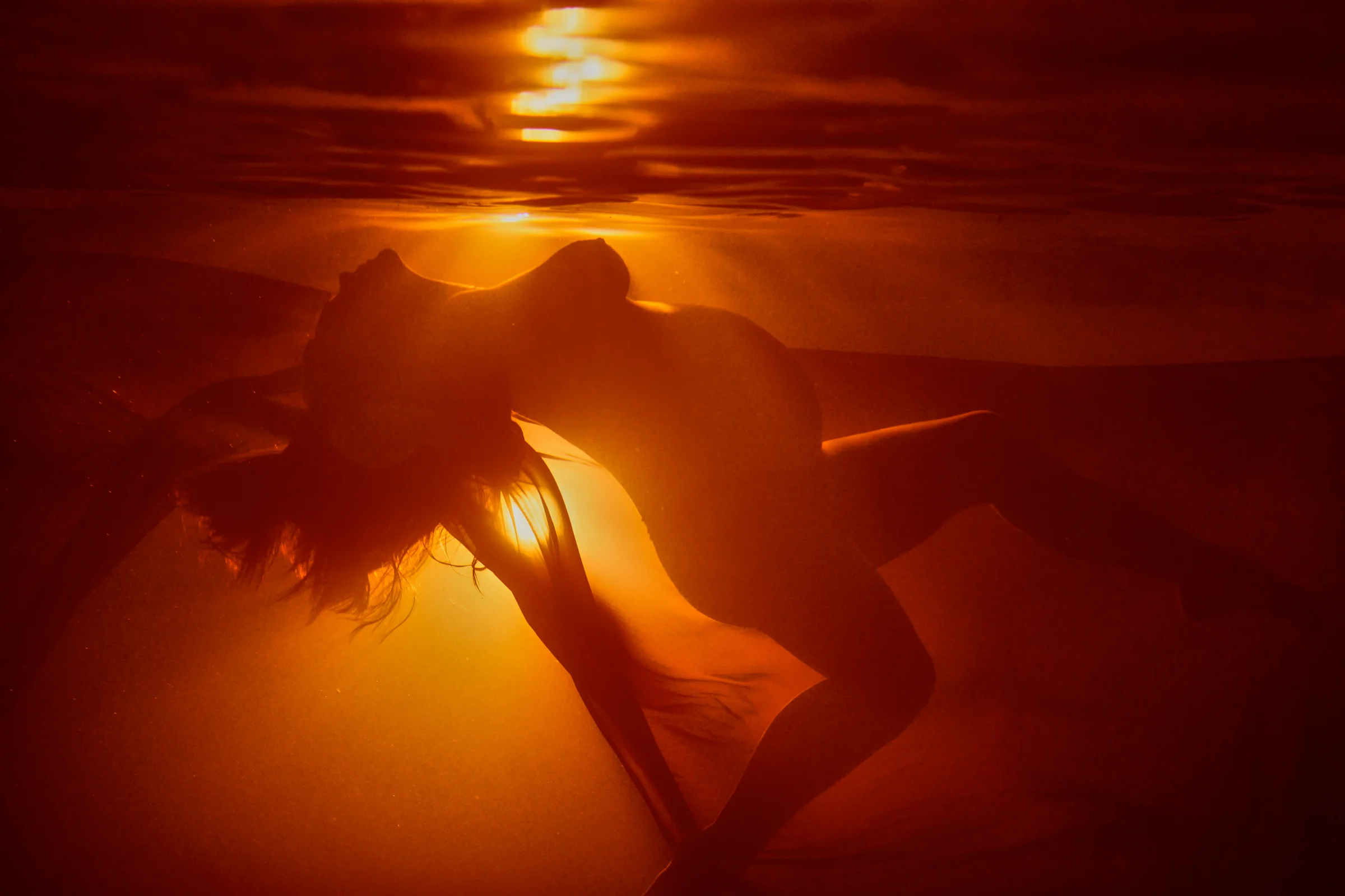 Underwater silhouette of a pregnant woman gracefully arching her back, illuminated by a golden glow.