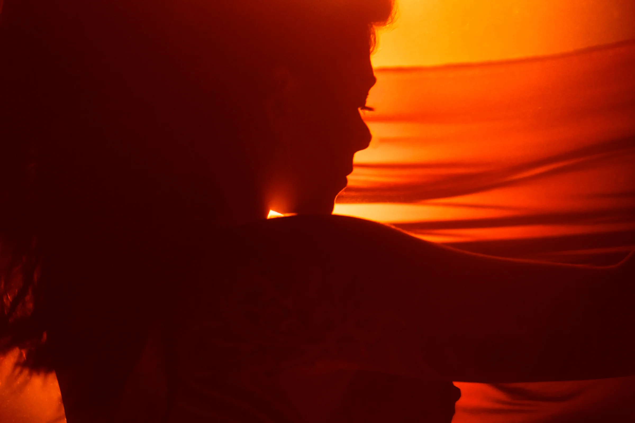 Silhouette of a woman’s profile, warmly illuminated by an orange glow with flowing fabric in the background.