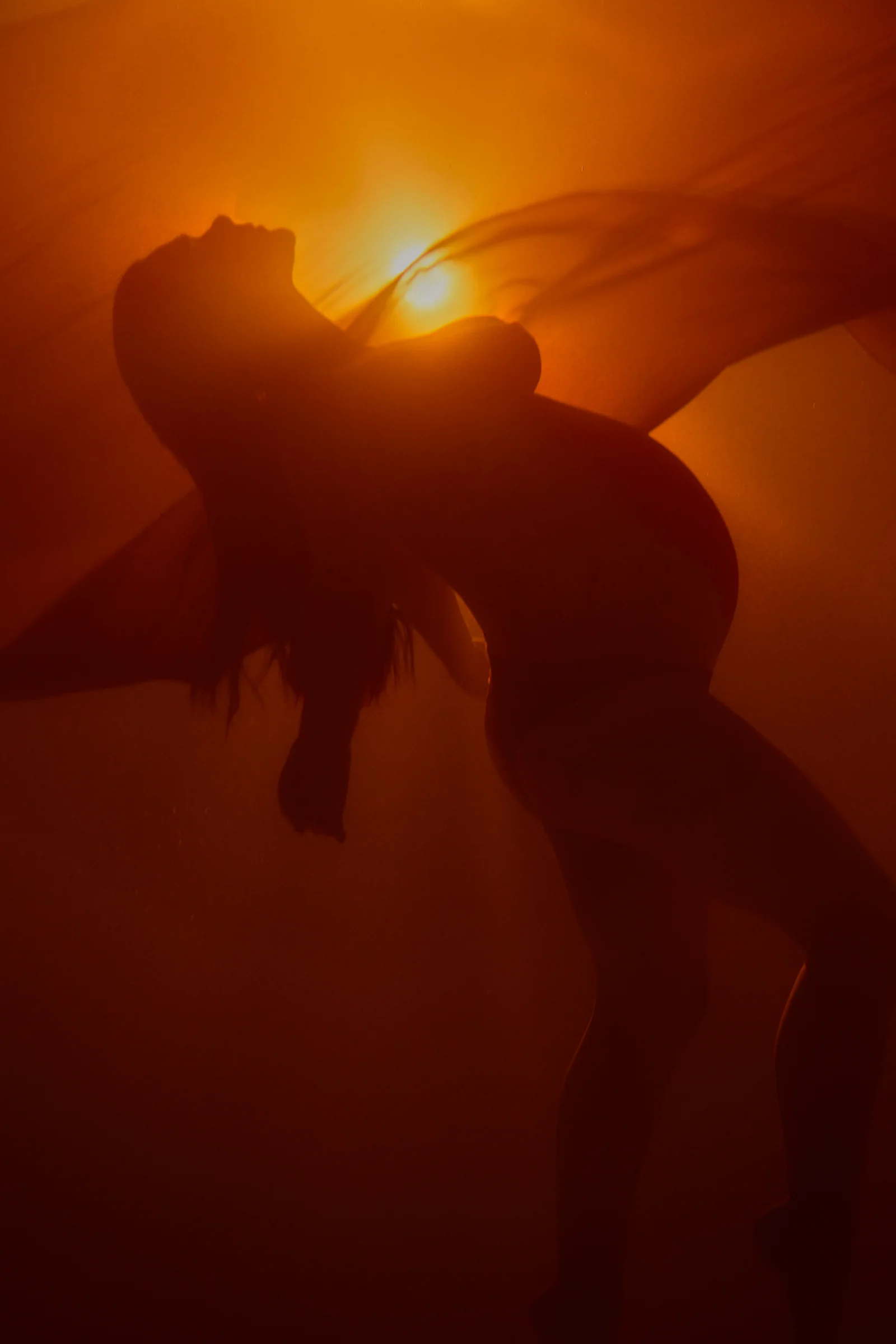 Silhouette of a pregnant woman underwater, illuminated by a warm, orange glow with flowing fabric accentuating her form.